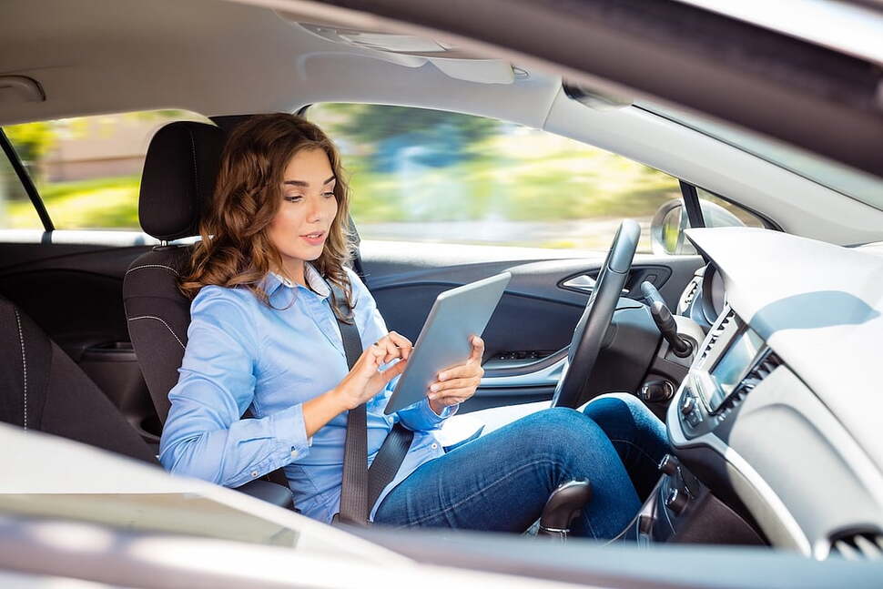 Cover photo of article depicting woman using a tablet in the drivers seat of a self-driving car